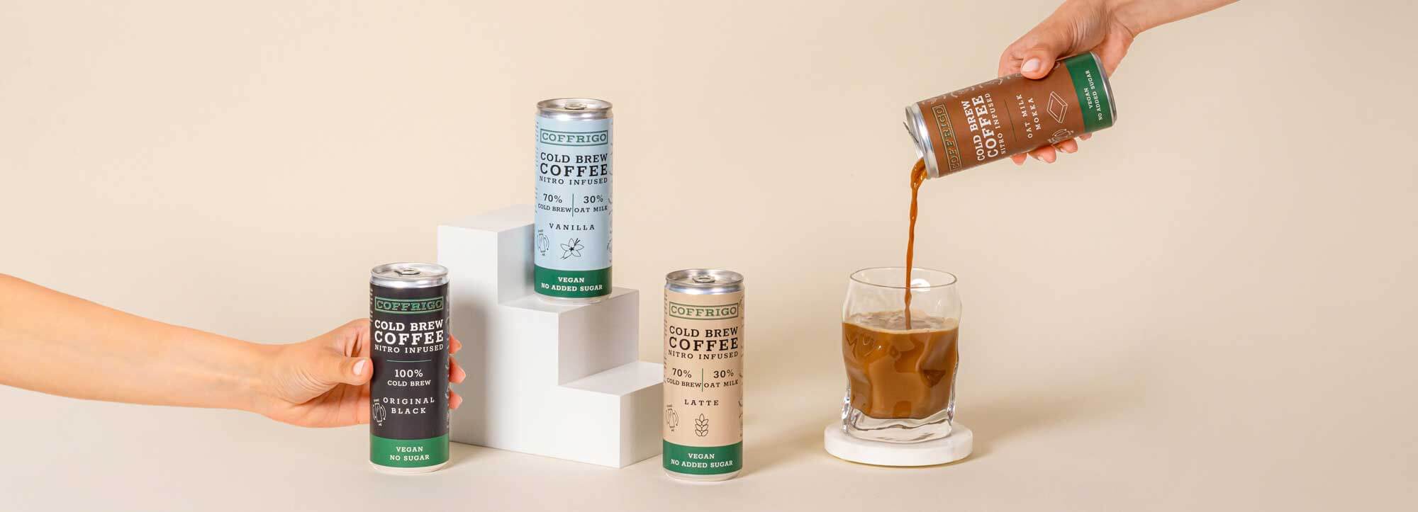 Vier Cold Brew Kaffee Dosen von COFFRIGO vor beigem Hintergrund. Eine dose OAT MILK VANILLA auf einem Podest, eine andere OAT MILK MOCCA wird in ein Glas eingeschenkt.